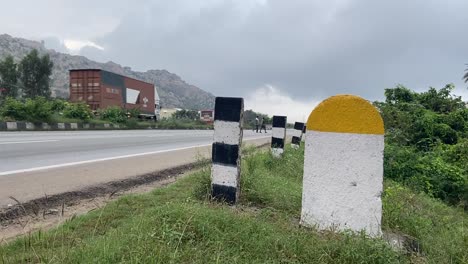 captured real photo of plain yellow and white milestone with national highway road and green plants background which can be used for writing kilometre numbers