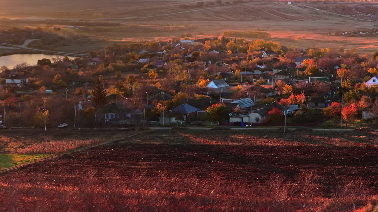 Aerial drone view of a Moldovan village surrounded by autumn trees and farmlands during sunset