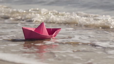 woman's hand places origami boat in the sea and it floats away