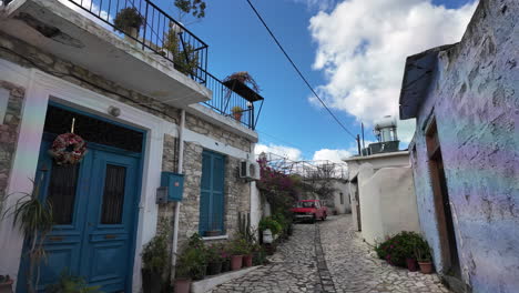 Charming-narrow-street-in-Lefkara-with-stone-houses,-potted-plants,-and-a-red-car