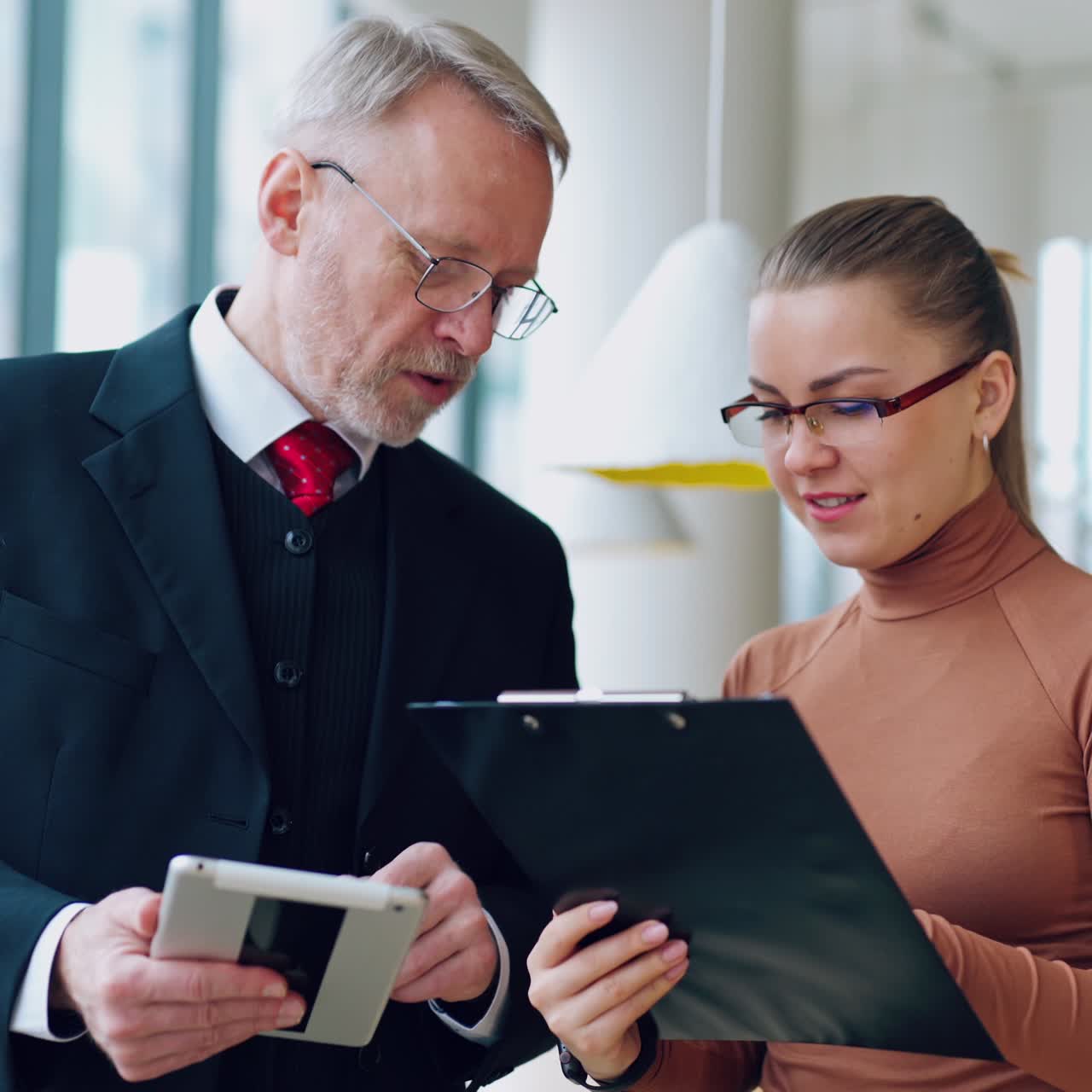 Senior man in costume and a young woman indoors. Serious businessman giving advice to his secretary in the company. Business concept.