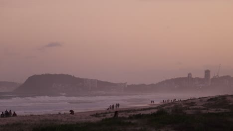 people strolling on beach at dusk, city in background