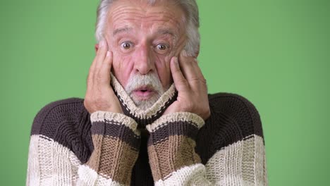 handsome senior bearded man wearing warm clothing against green background