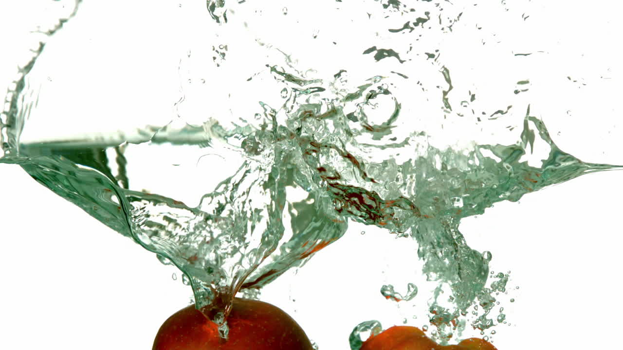 mitades de manzana sumergiéndose en el agua sobre un fondo blanco