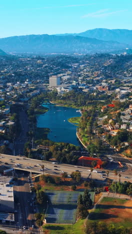 approaching the beautiful little lake in the residential area of los angeles. busy traffic in the green part of the city at backdrop of mountains. vertical video