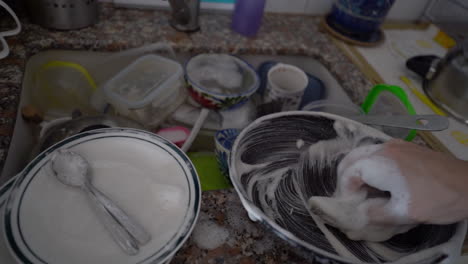 a man's hands clean a pan in a sink full of dirty dishes