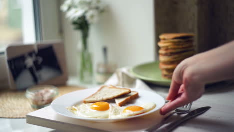 Woman-put-plate-with-fried-eggs-and-slices-of-toast-bread-on-kitchen-table