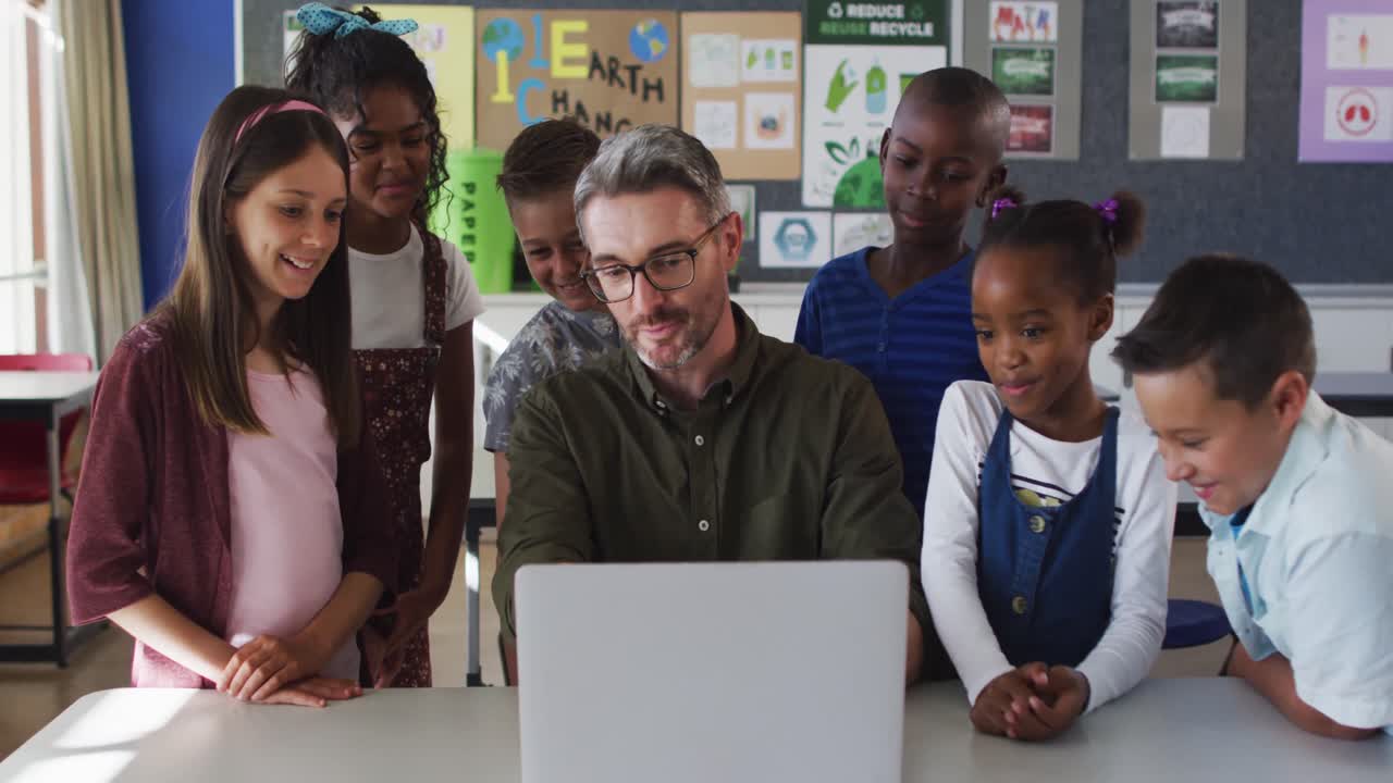 Diverse male teacher and group of schoolchildren looking at laptop