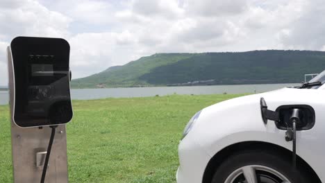 progressive concept of ev car with green field, hill and lake as background.