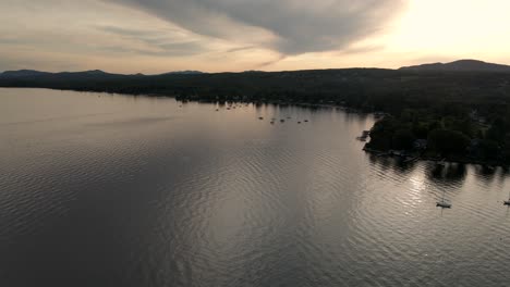 boats sailing on a calm water with mountain silhouette and sunlight in memphremagog lake beach, magog, quebec, canada