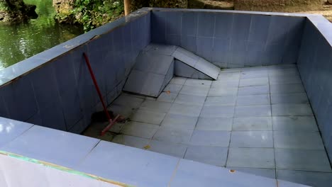 pan rechts van een leeg zwembad naast het water, buiten gebruik tijdens onderhoud vieze tegels schoon te maken met rode borstel