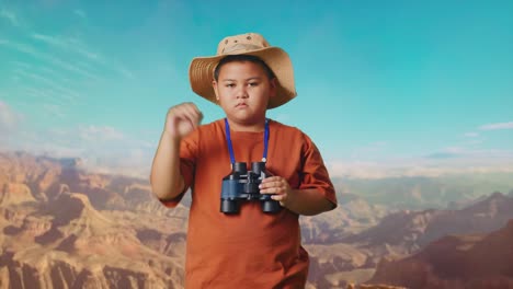 asian boy with a hat showing thumbs down gesture after looking through the binoculars. boy researcher examines something while traveling at the top of mountain, travel tourism adventure concept
