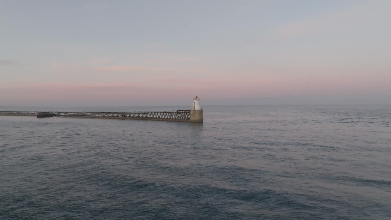 Drone clip showing calm sea to the horizon, with traditional lighthouse and harbour wall