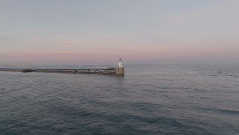 drone clip showing calm sea to the horizon, with traditional lighthouse and harbour wall