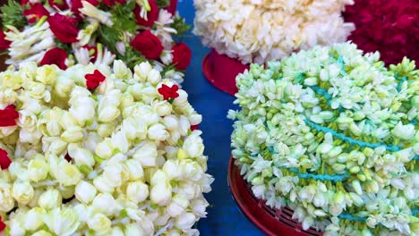 camera slowly pans over vibrant jasmine and rose flower garlands arranged on a blue table in natural daylight at a singapore market
