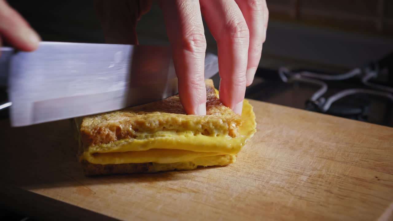 un primer plano de las manos de un chef colocando un sándwich antes de cortarlo por la mitad con un cuchillo de cocina, el sándwich cocido de tocino, huevo y queso se coloca para su presentación