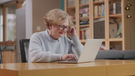 happy older lady searching for something on tablet laptop while sitting at table in cozy apartment: close up shot