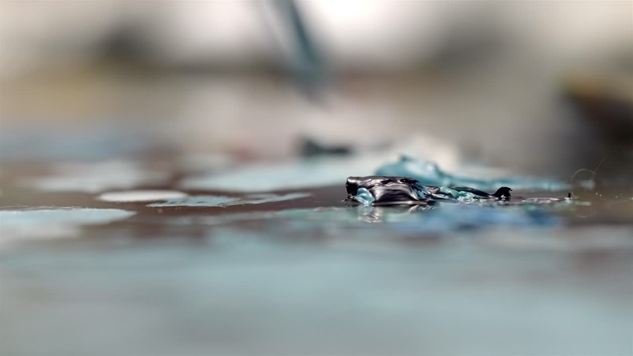Kuas seniman mendekati cat biru di atas kanvas dengan bokeh lembut, menciptakan suasana yang mengalir.