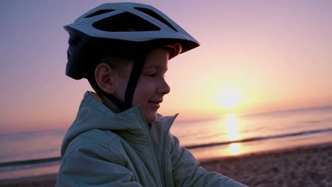 young boy in a helmet enjoying the sunset at the beach