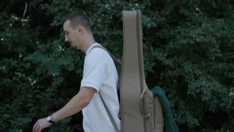 young man walking with guitar on street near forest