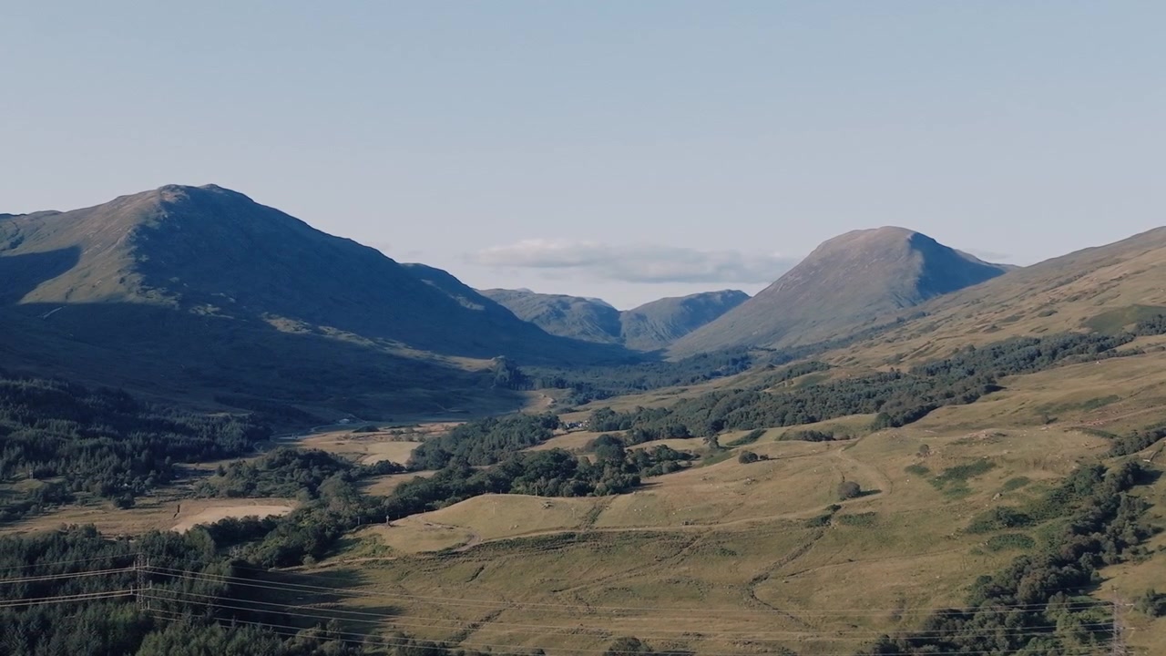 Veduta aerea di una valle verde con campi coltivati a mosaico che si estendono verso una lontana catena montuosa.
