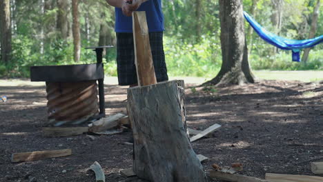 Slow motion, man chopping wood in half on tree trunk while camping