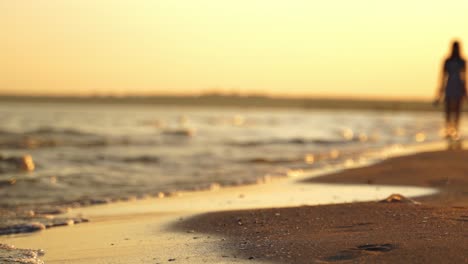 edge of sea with waves on sand shore. silhouette of the woman walking on shoreline on the water background in the evening.