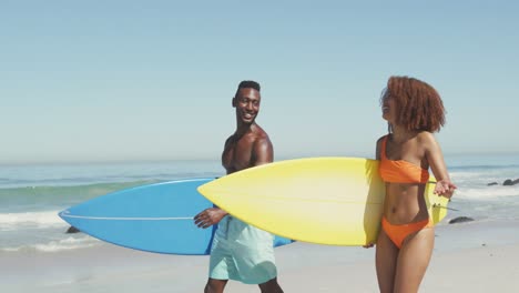 african american couple walking and holding surfboards