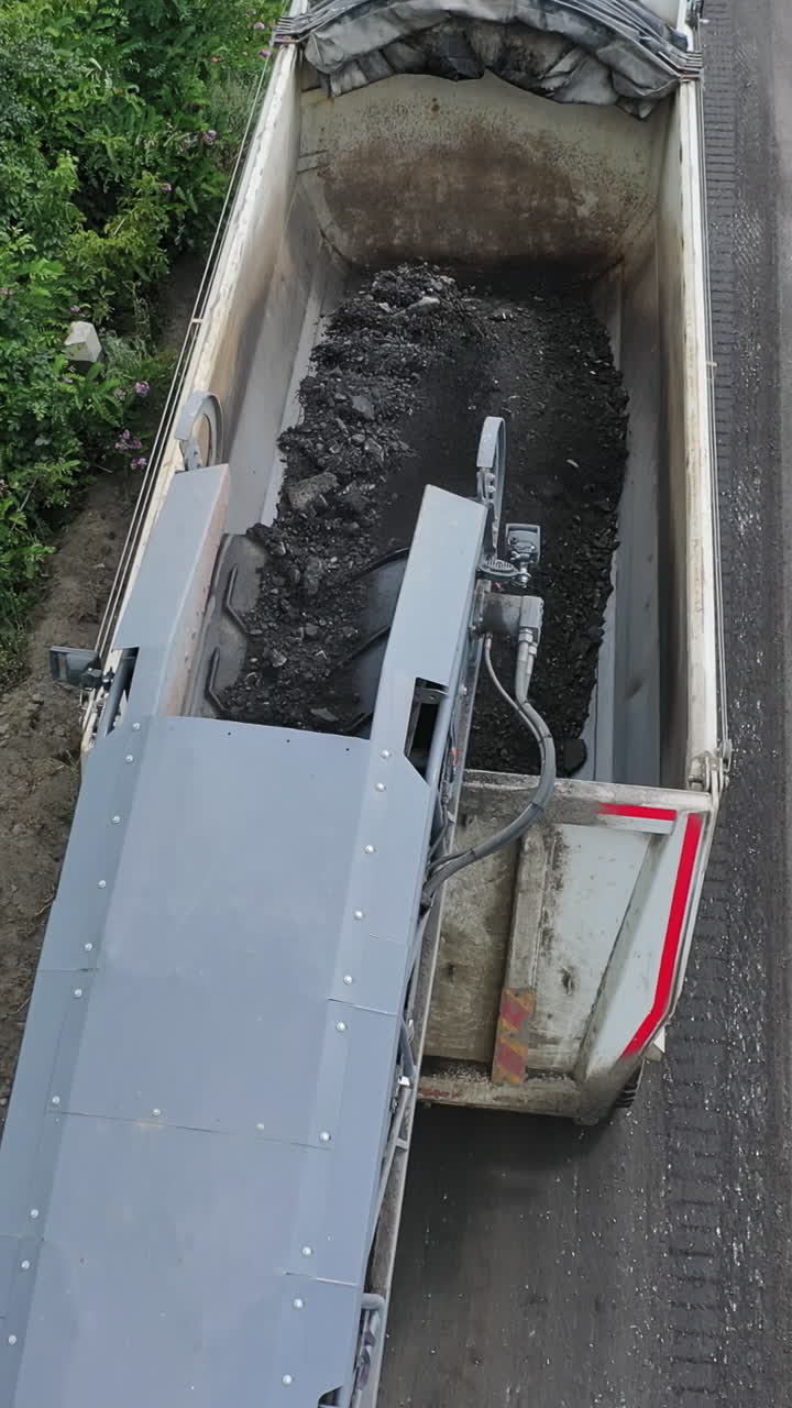 Heavy machinery at roadworks. Special machinery loading truck with asphalt on the road. Reconstruction on the highway. Aerial view. Vertical video