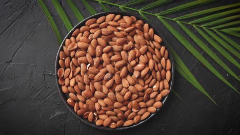 composition of whole almond nuts in black plate placed on black stone table