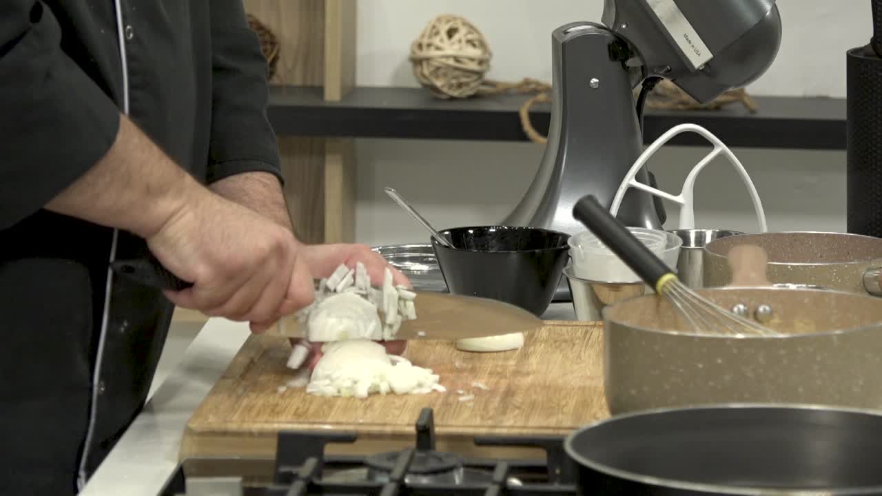 Cooking expert skillfully chops garlic and prepares ingredients in a stylish kitchen filled with essential cookware and tools. The focus is on precise technique and presentation