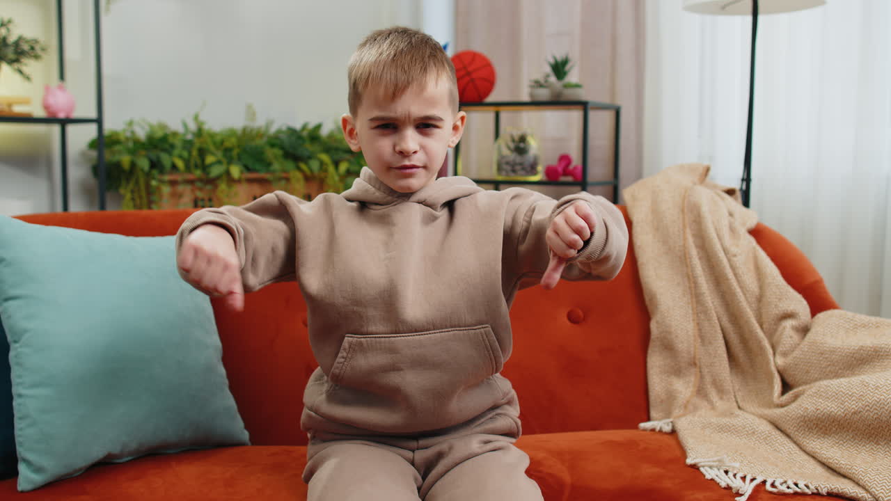 Upset teen boy showing thumbs down dislike bad work disapproval dissatisfied feedback at home