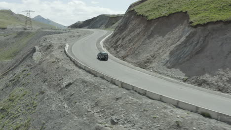 a car drives along a winding mountain road in kyrgyzstan with rocky terrain nearby