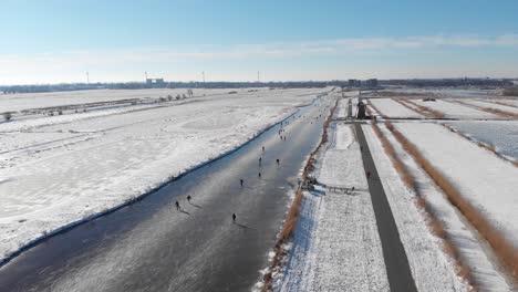 Dutch-locals-ice-skating-on-frozen-countryside-canals,-winter-aerial-landscape