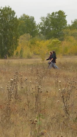 couple of girls walks on meadow near village under clear sky. teenagers in medieval clothes talk holding bags and map to orientate area side view