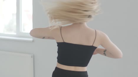 fit girl in black clothes performing contemporary. female dancer shows flowing motions, body and hands waves at white room. modern ballet dance choreography. young woman is moving smoothly