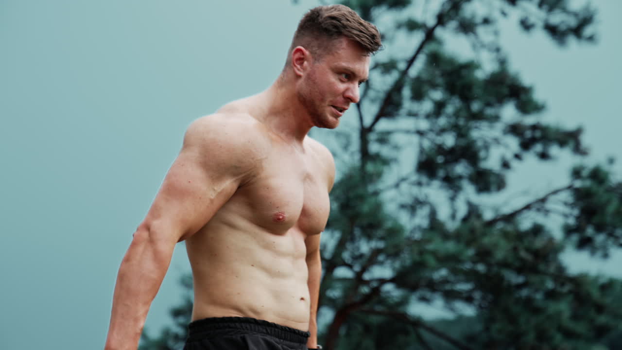 Muscular Caucasian man with naked torso showing his strong muscles. Sportive guy exercising outdoors.