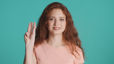 una chica pelirroja mirando a la cámara sobre un fondo turquesa.