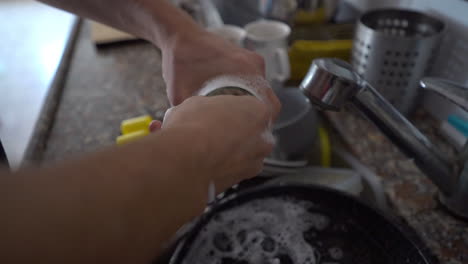 a man washes a glass with a soapy sponge above a sink full of dirty dishes