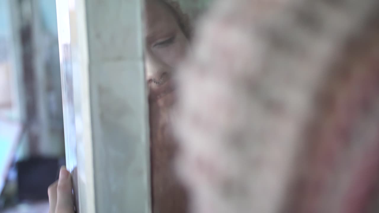 문신과 비니를 쓴 젊은 여성은 유리 모자이크 벽에 비친 자신의 모습을 마주하고 부드럽고 느리고 관능적으로 춤 동작으로 위아래로 움직이며 재미있고 우스꽝스러운 표정을 짓습니다.