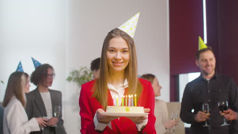 Porträt-Einer-Schönen-Frau,-Die-Einen-Geburtstagskuchen-Hält-Und-Während-Einer-Party-Im-Büro-In-Die-Kamera-Schaut