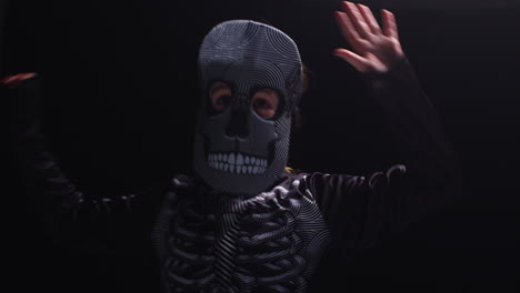 studio shot of child dressed up in skeleton costume trick or treating at halloween dancing against black background 4