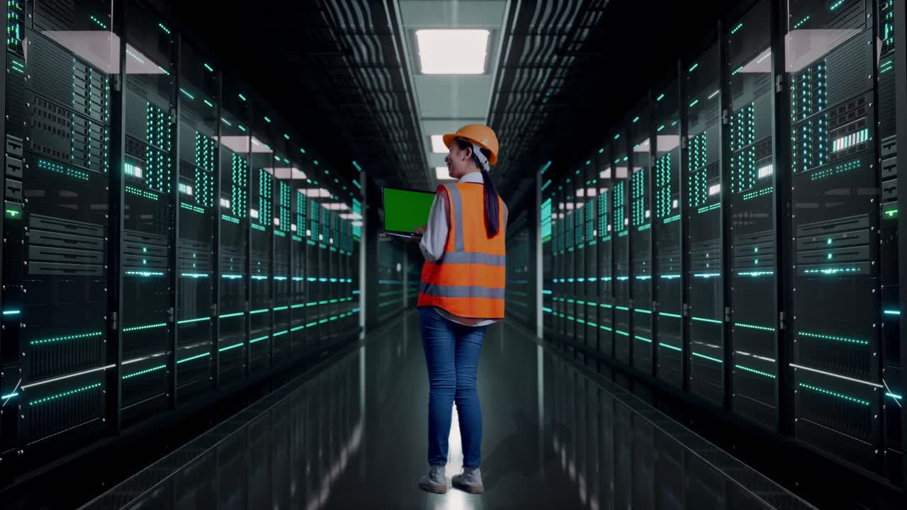 Full Body Back View Of Asian Female Engineer With Safety Helmet Working A Green Screen Laptop in Server Room Data Center