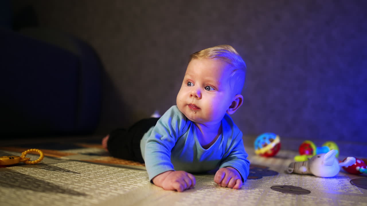 Little infant baby with fair hair lies on his belly. Peaceful baby boy looking up with interest.