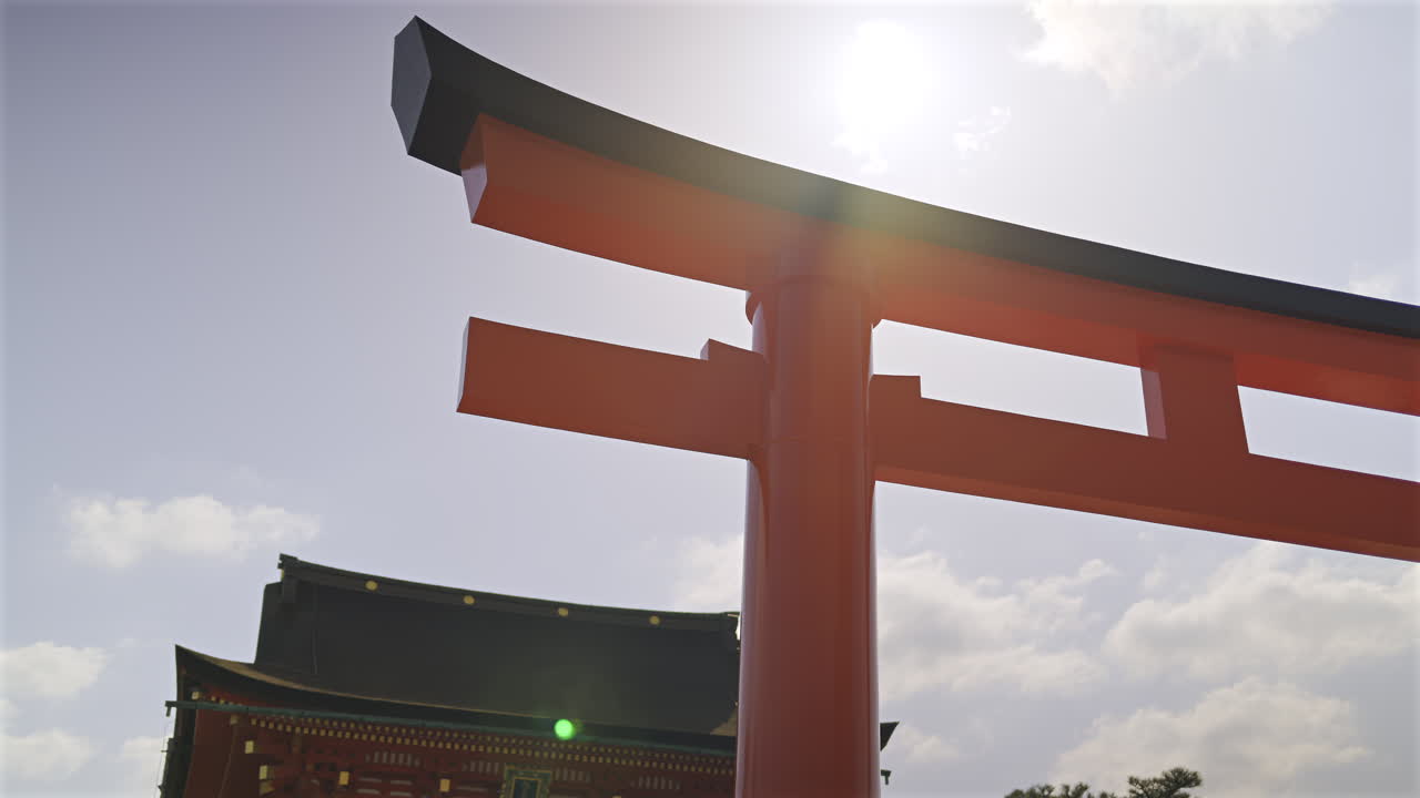 Bright red gates of Fushimi Inari traditional shrine stand tall against a clear sky with sun