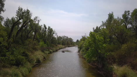drone shot of a river surrounded by green forest featuring a canoe