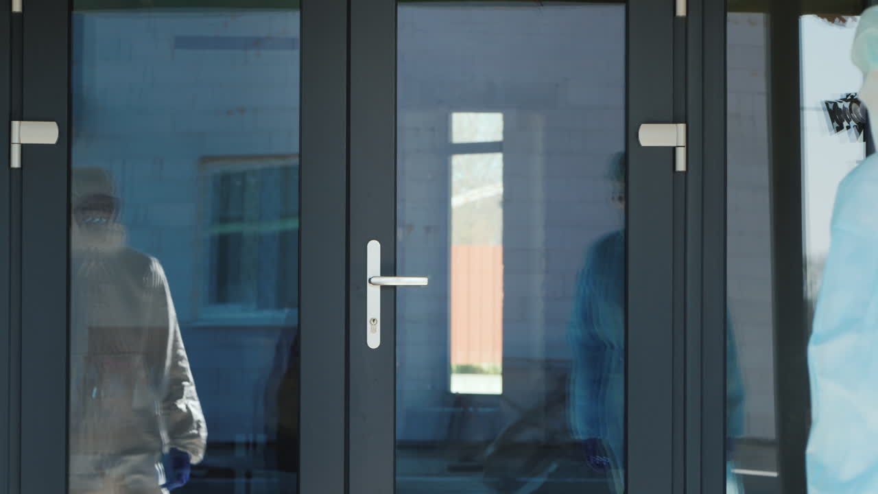 un grupo de médicos con trajes protectores se comunica con una anciana en la puerta de su casa