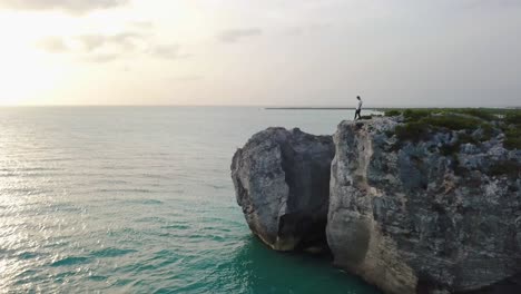 Macho-Joven-Caminando-A-Lo-Largo-De-Un-Acantilado-Rocoso-En-El-Océano-En-Providenciales-En-El-Archipiélago-De-Turcas-Y-Caicos-Al-Atardecer