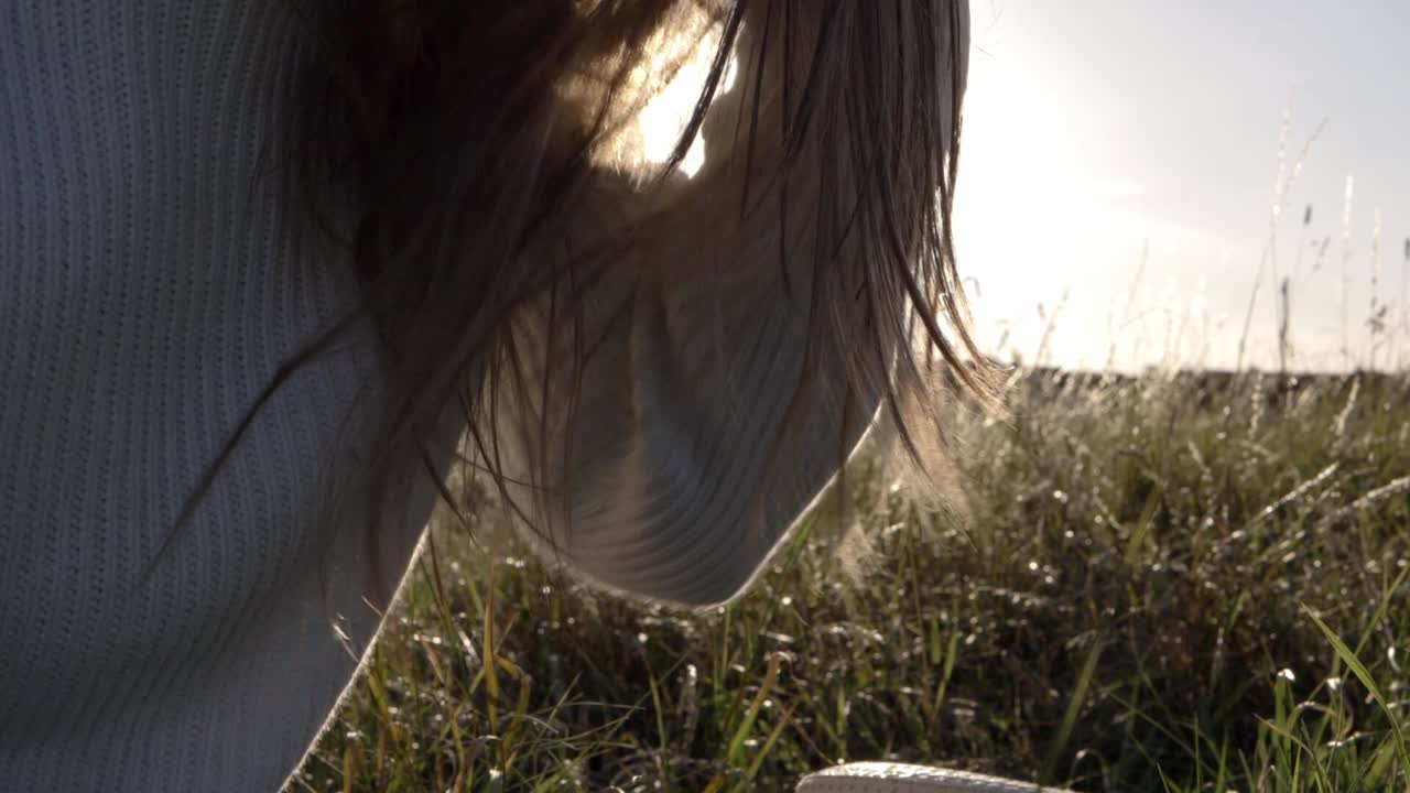 Woman playing with her long hair against sunshine background close up shot