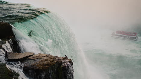 Die-Berühmten-Niagarafälle,-Weit-Unten-Fährt-Ein-Schiff-Mit-Touristen.-Sehenswürdigkeiten-Von-Amerika.-4K-Video-In-Zeitlupe